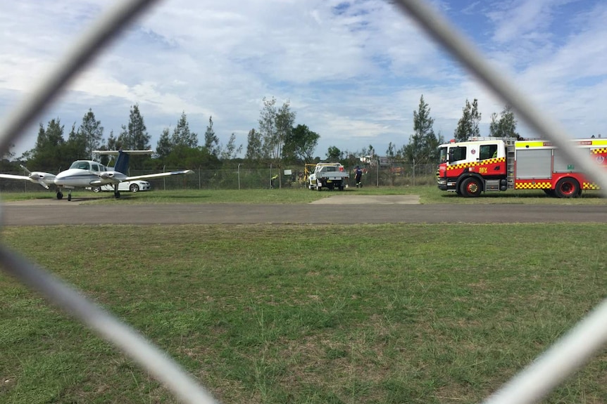 Several people, and emergency service vehicles in the distance, surrounded by trees.