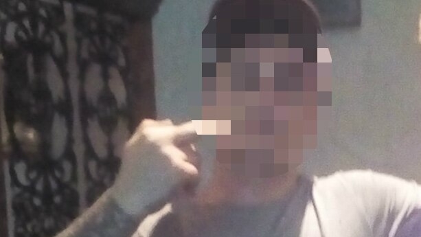 A man makes a hand gesture as he poses for a photo, his face is pixellated