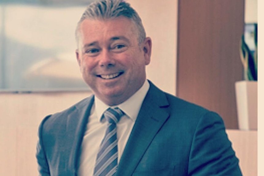 A middle-aged man with grey hair, smiling, wearing a suit.