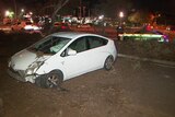 A badly damaged white car in dirt with a police on the road behind