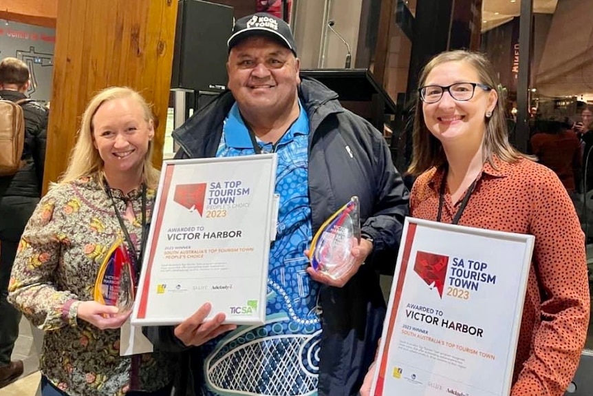 Two women and a man display certificate of awards