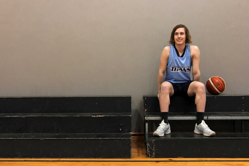 Young man sitting on stands with basketball beside him