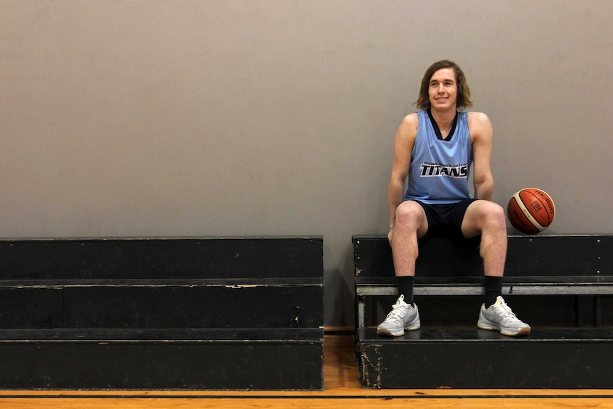 Young man sitting on stands with basketball beside him