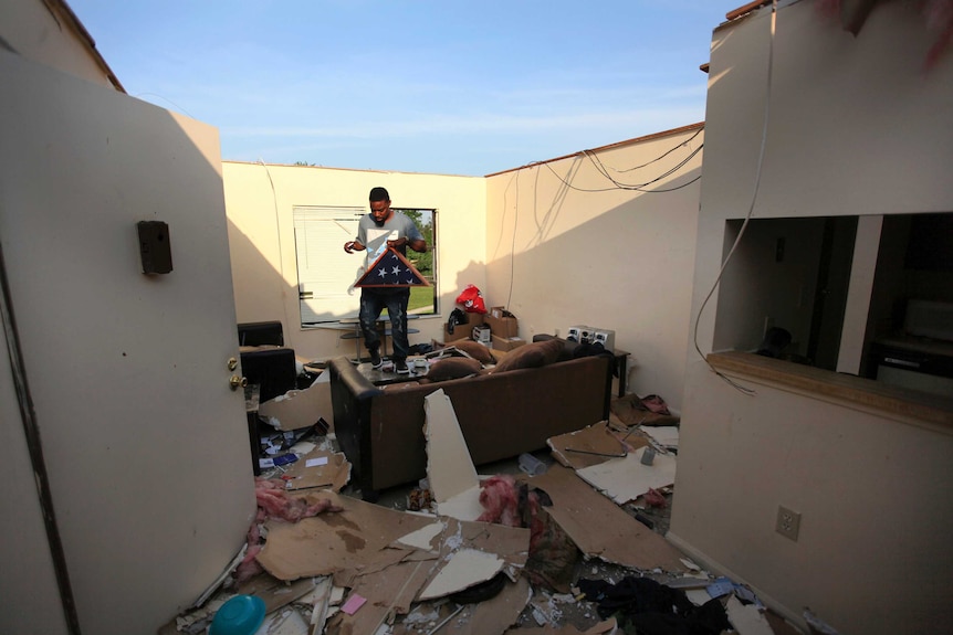 A man carried a folded up flag through a debris-strewn house without a roof.