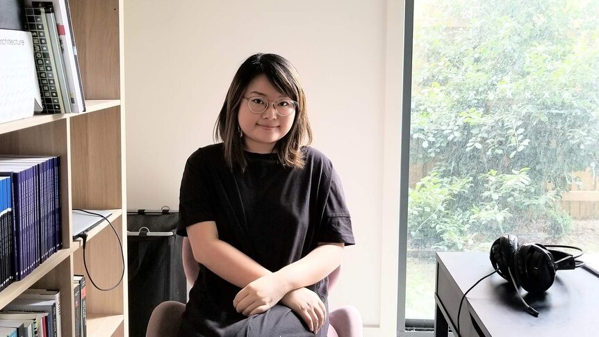 Sarah Ouyang, wearing a dark top, sits next to a bookcase inside.