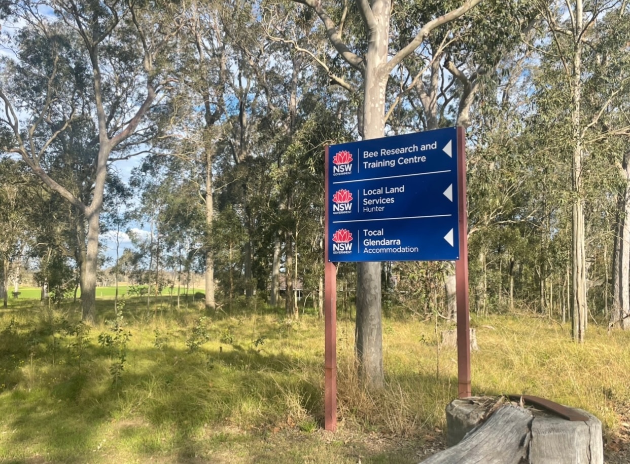A blue sign in the middle of a paddock reads "bee research and training center" with an arrow in its direction.