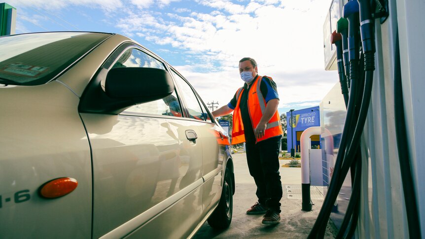 A man in a high-vis vest stands with his car at a petrol station.