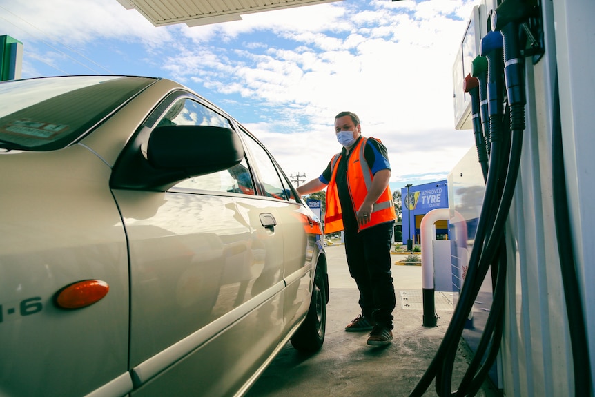A man in a high-vis vest stands with his car at a petrol station.