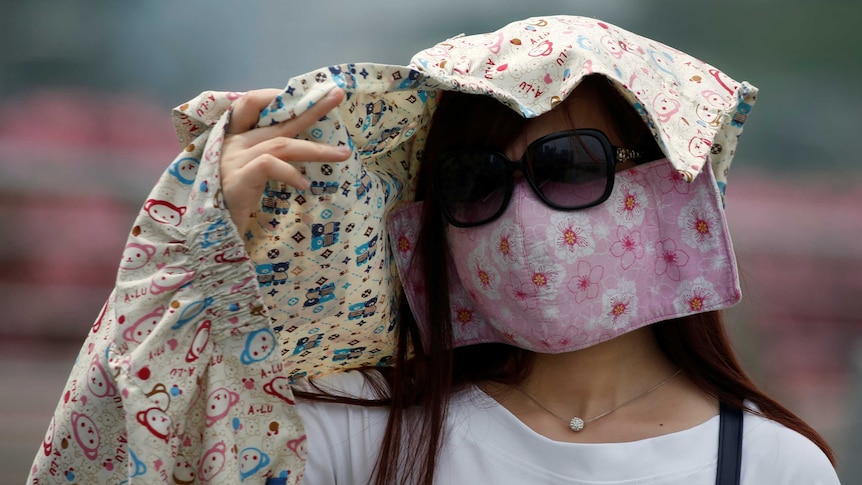 A woman wearing a face mask shields her face.