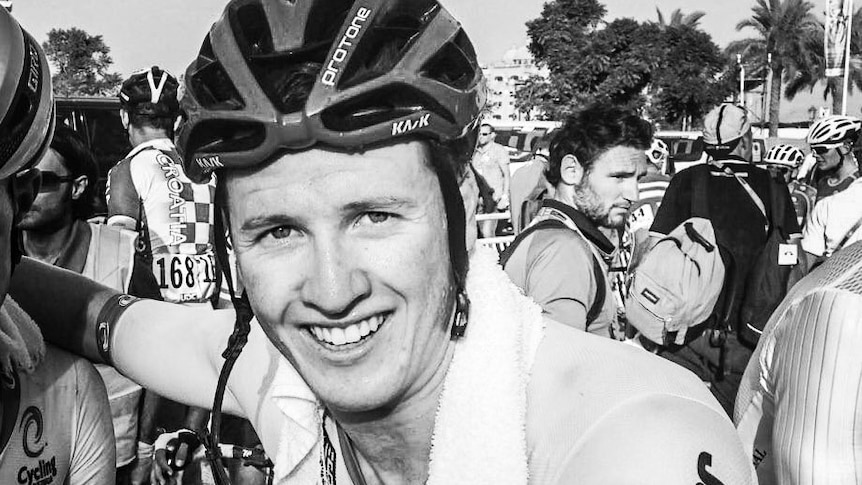 A close-up black and white photo of cyclist Jason Lowndes looking at camera wearing helmet