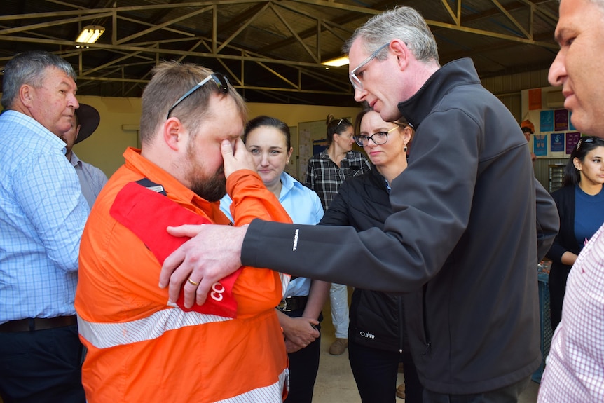 a man wearing glasses consoling another man who is a ses volunteer during the flooding crisis