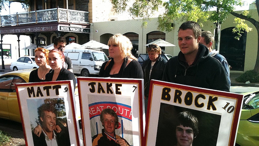 Families of three road smash victims hold posters outside court