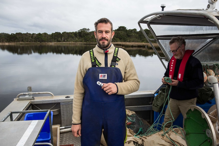 A man holds a tracking device. He is standing in the back of a boat