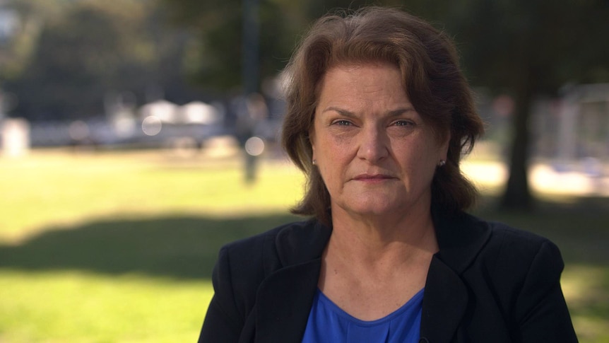 A woman with a neutral expression looks at the camera sitting in a park.