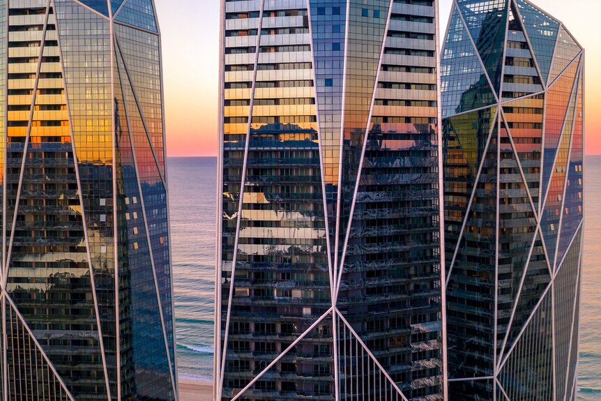 a close-up aerial shot of three beachfront residential towers with an all glass exterior