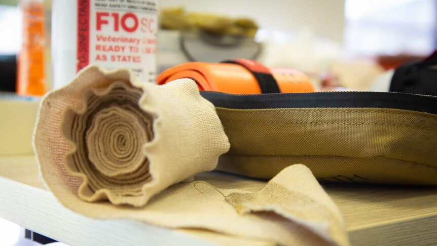 A compression bandage sits on a table among other first aid materials.