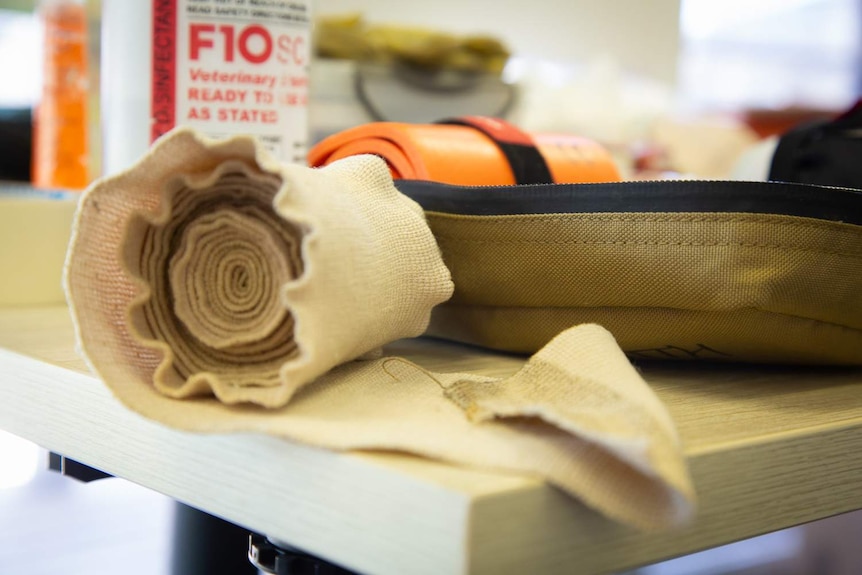 A compression bandage sits on a table among other first aid materials.