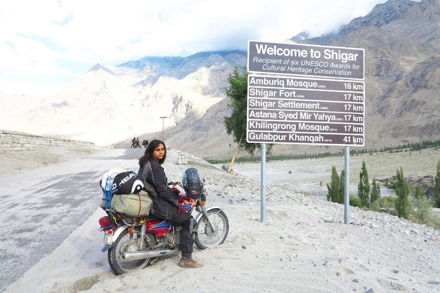 Zenith on her motorbike poses next to 'Welcome to Shigar' sign