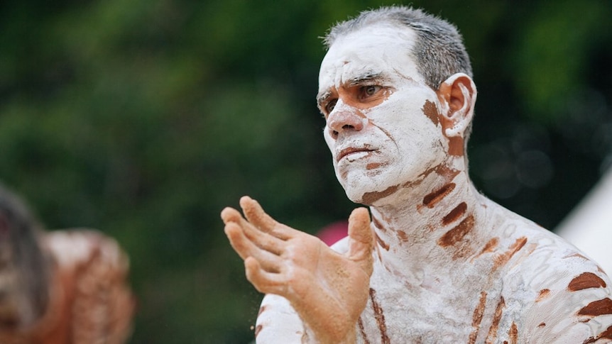 An Aboriginal man with short hair performs a traditional dance.