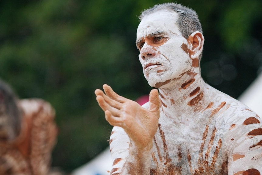 An Aboriginal man with short hair performs a traditional dance.