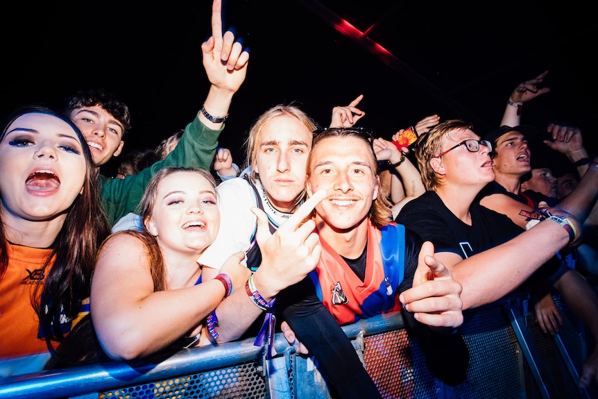 A bunch of young people celebrate while leaning on a stage barricade