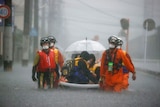 Rescuers in orange protective wear walk in knee deep water to save residents with umbrellas.