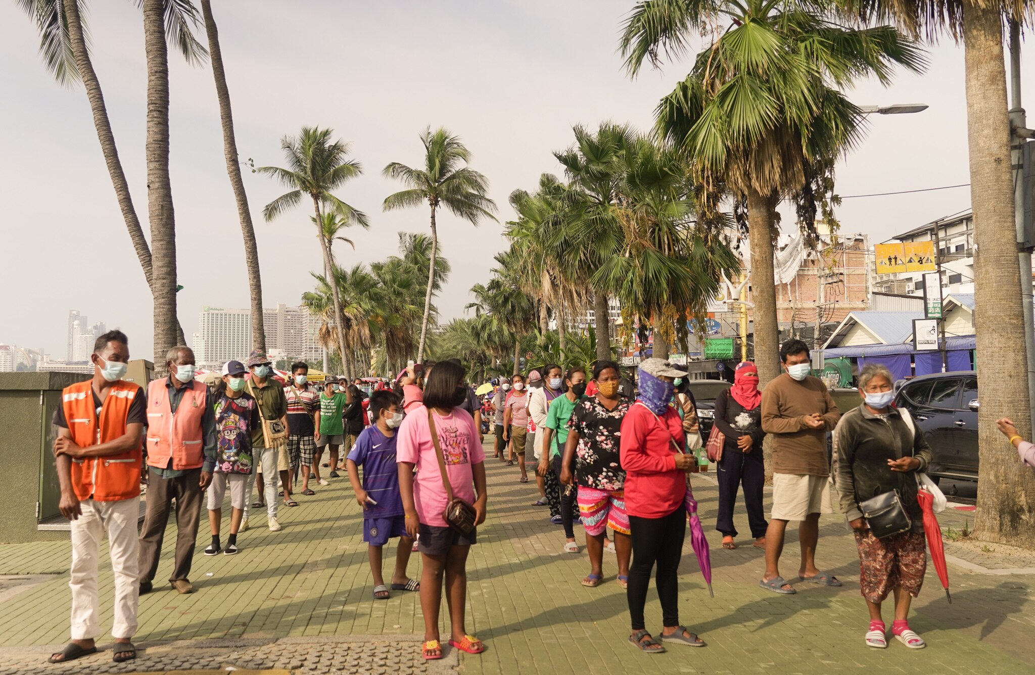 A group of people wearing masks stand in a line with palm trees on either side.