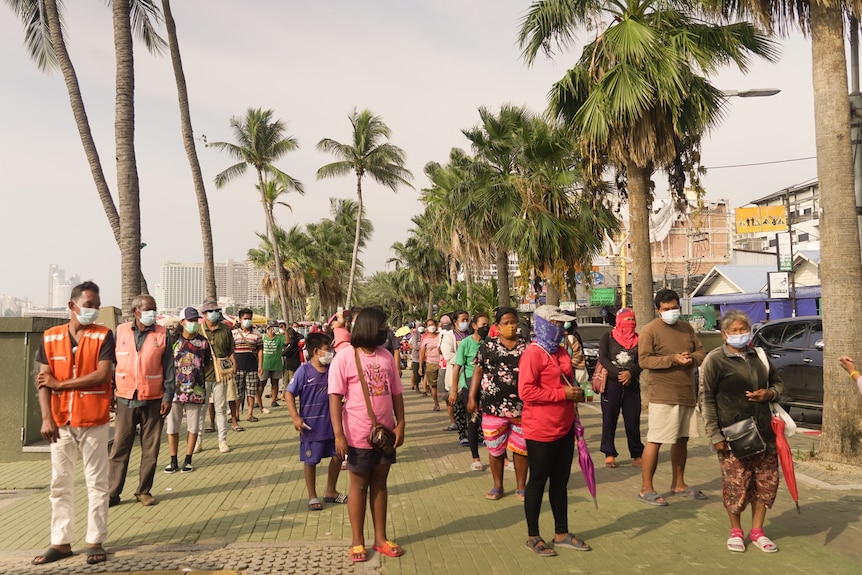 A group of people wearing masks stand in a line with palm trees on either side.