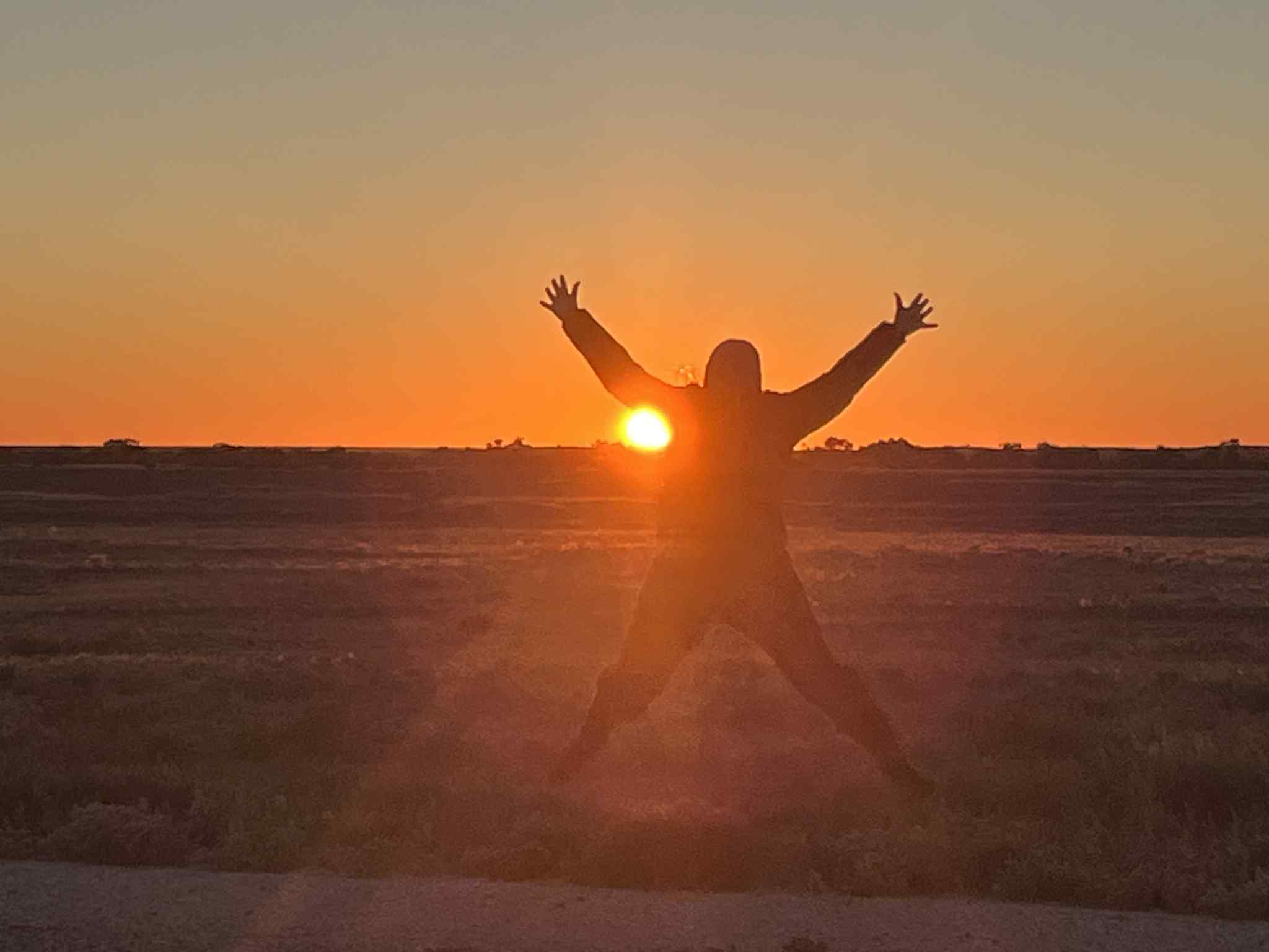 Una silueta saltadora en forma de estrella contra una puesta de sol dorada. 