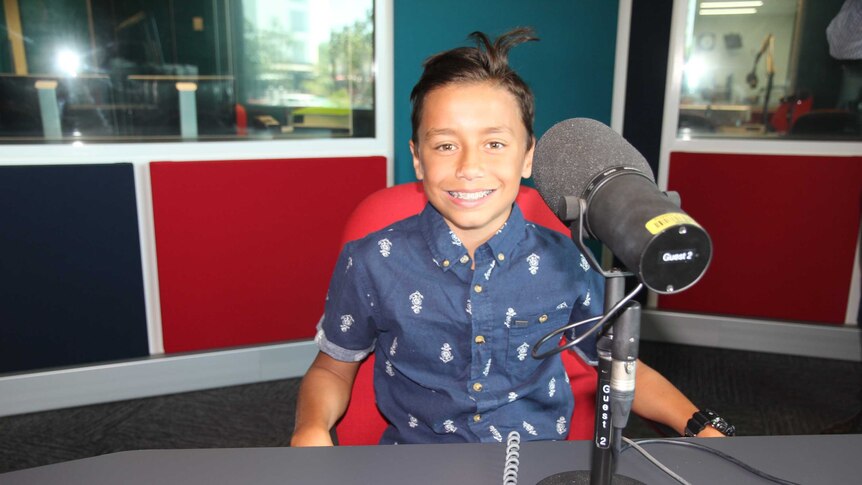 A young boy in a radio studio behind a microphone.