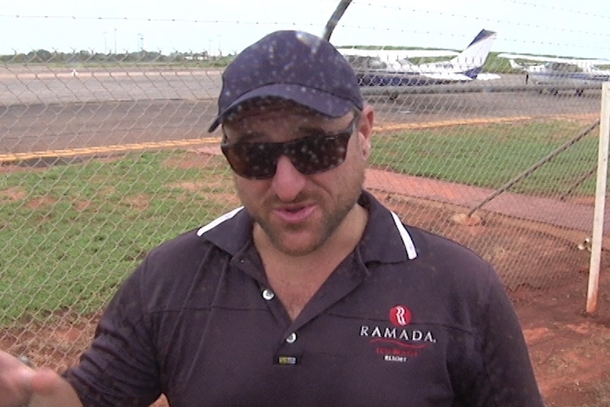 A man wearing a cap stands in the rain near an airport.