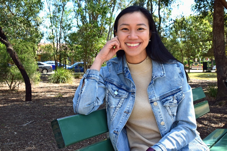 A woman wearing a denim jacket sits on a park bench.