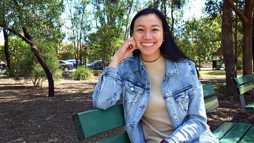 A woman wearing a denim jacket sits on a park bench.