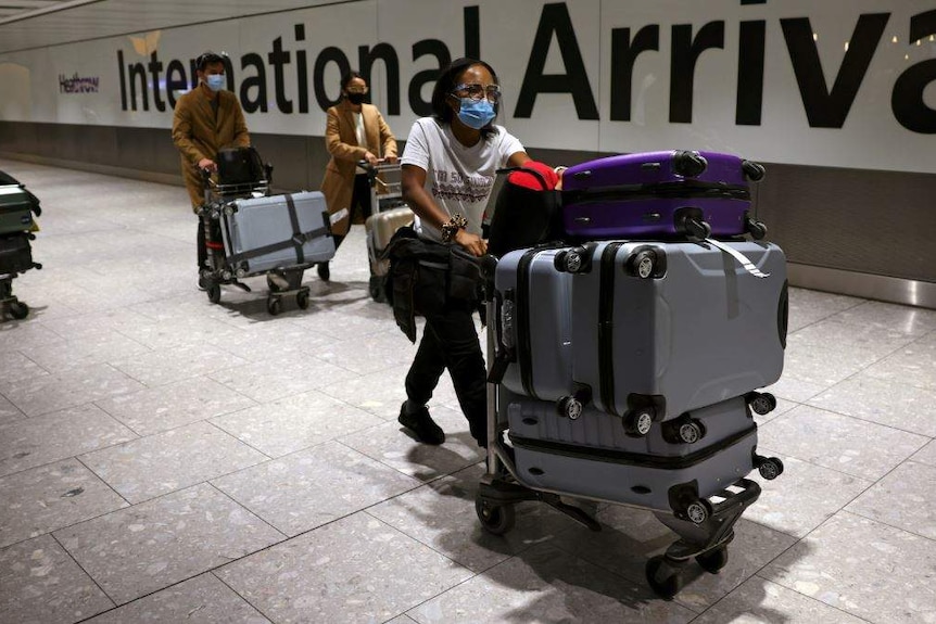 People pushing bags and wearing masks walk past an international arrivals signa t Heathrow Airport.