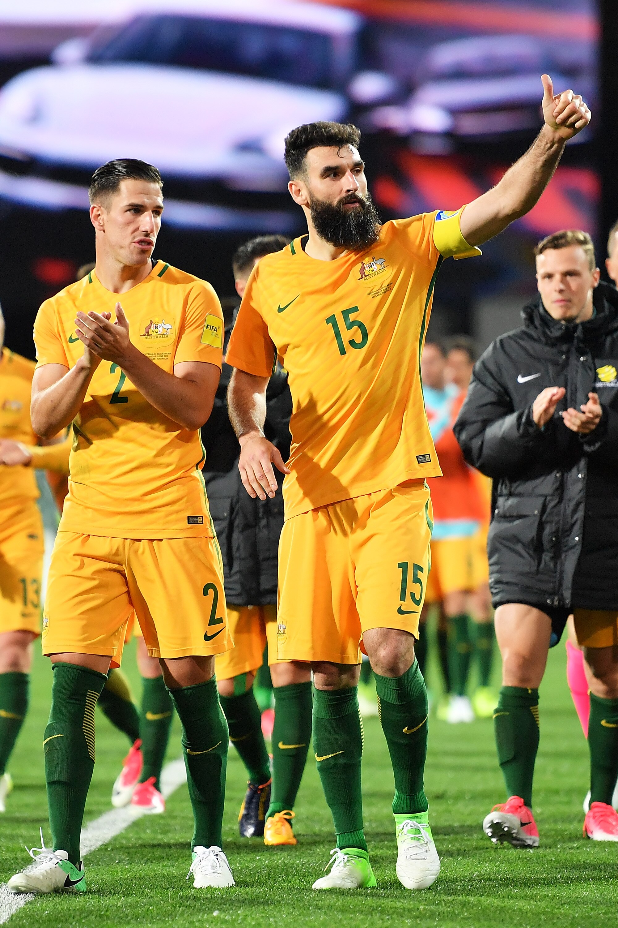 Two male soccer players wearing yellow clap to the crowd after a game while one holds up his thumb