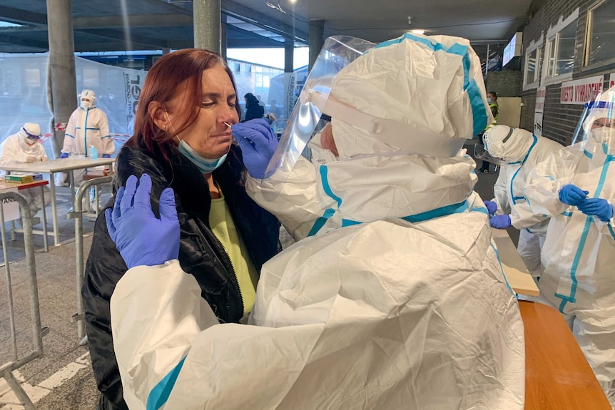 A woman closes her eyes while a health worker in full PPE inserts a swab into her nose