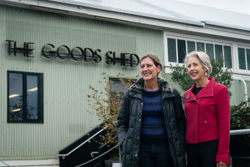 Two women in front of green shed.