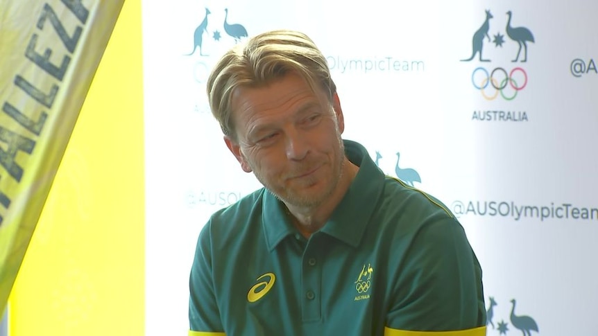 A man in a green and gold polo shirt speaks during a media conference about the Olympics.