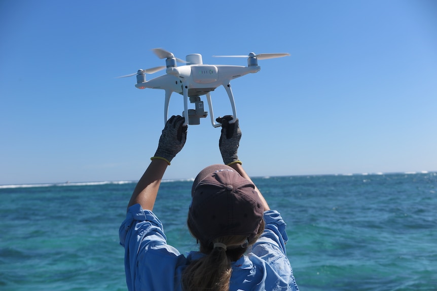 A woman releases a drone near the ocean