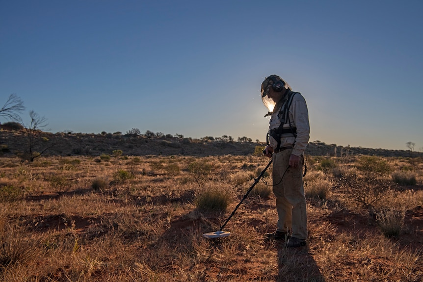 Man using metal detector in the Simpson Desert at sunset