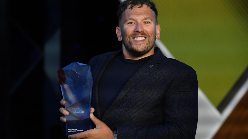 Brunette man in dark suit holds award