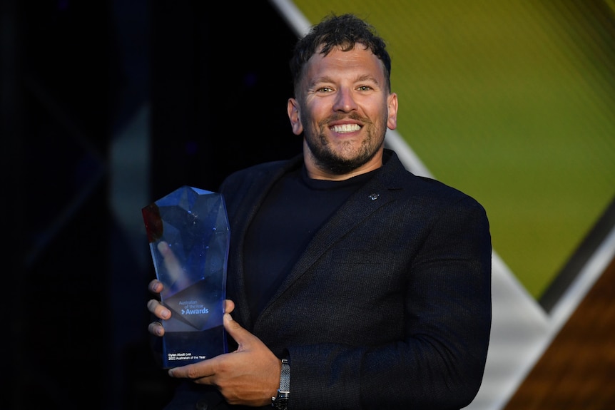 Brunette man in dark suit holds award