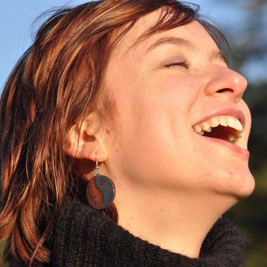 Close up shot of a woman with dark hair and a black roll neck jumper with her face to the sky, eyes closed, laughing