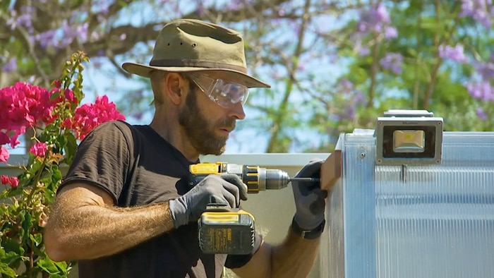 Man in hat and safety glasses using drill to attach timber to a greenhouse