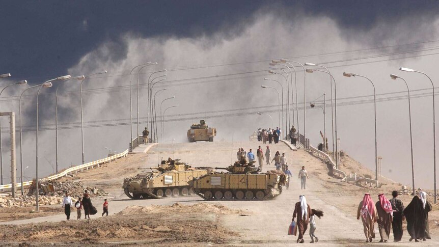 Iraqi civilians pass tanks on a bridge in Basra