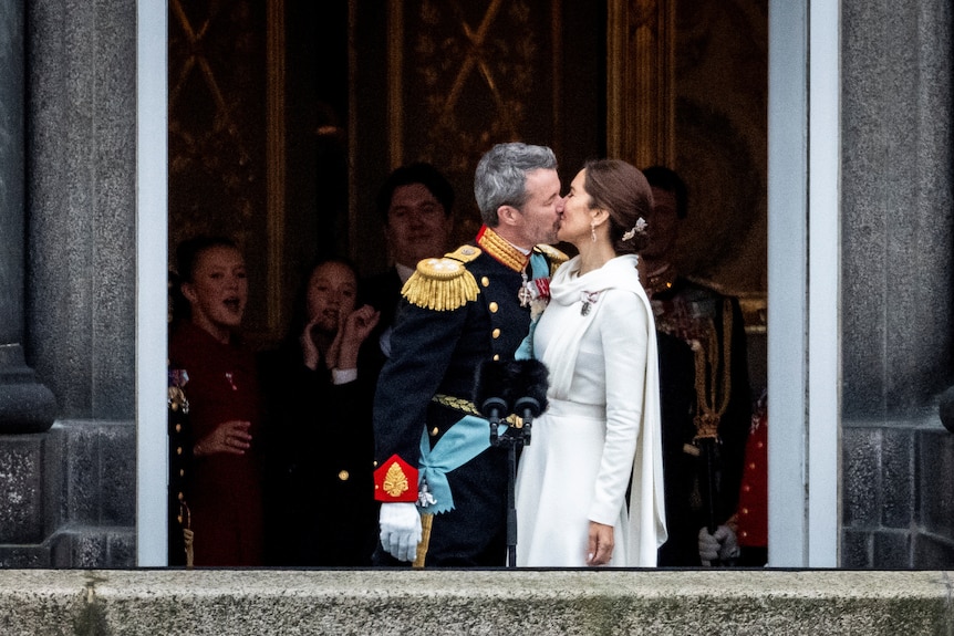 King Frederik and Queen Mary kiss while standing on a balcony