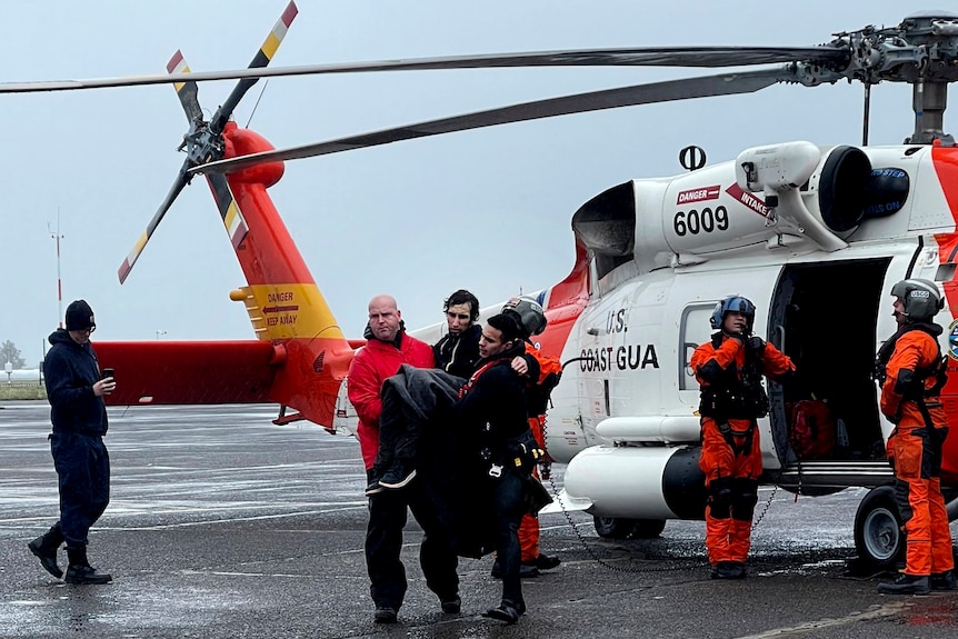 Coast Guard personnel help carry a swimmer from a rescue helicopter.