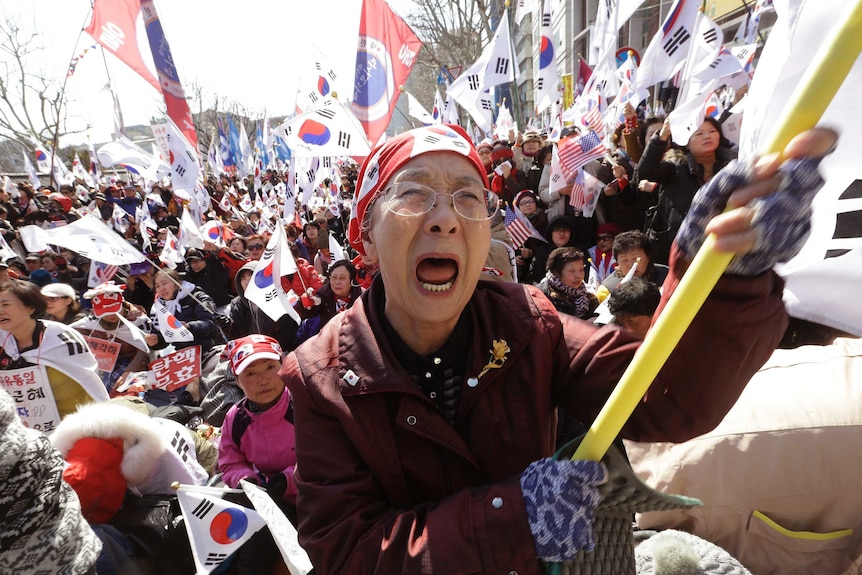 A supporter of South Korean President Park Geun-hye cries in front of a crowd of people holding flags at a rally.
