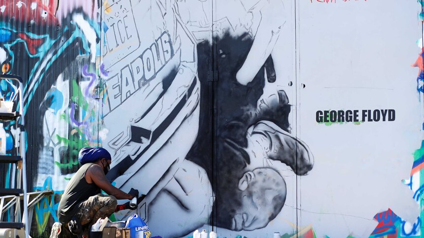 A man painting a mural showing police kneeling on George Floyd's neck with words, "I can't breathe' painted on the wall.