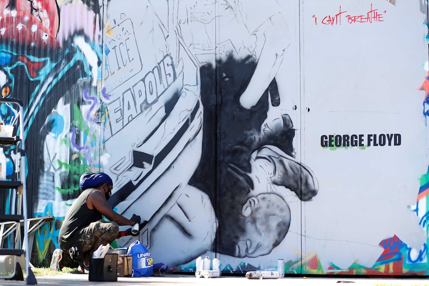 A man painting a mural showing police kneeling on George Floyd's neck with words, "I can't breathe' painted on the wall.